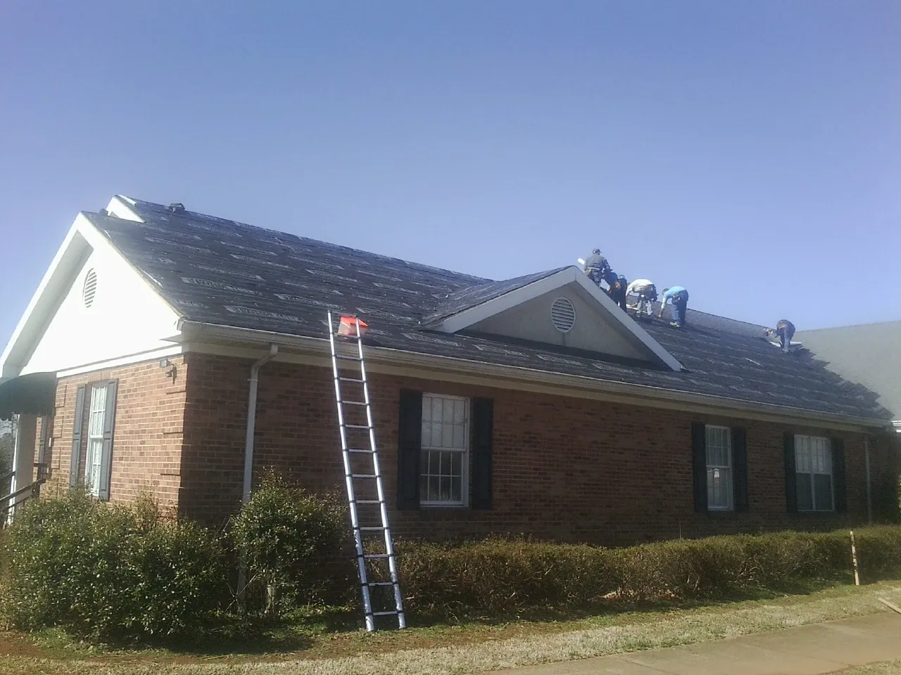 Crew tearing shingles off a brick ranch roof with a ladder set — Metal Roof Repair work by our crew in Woodburn