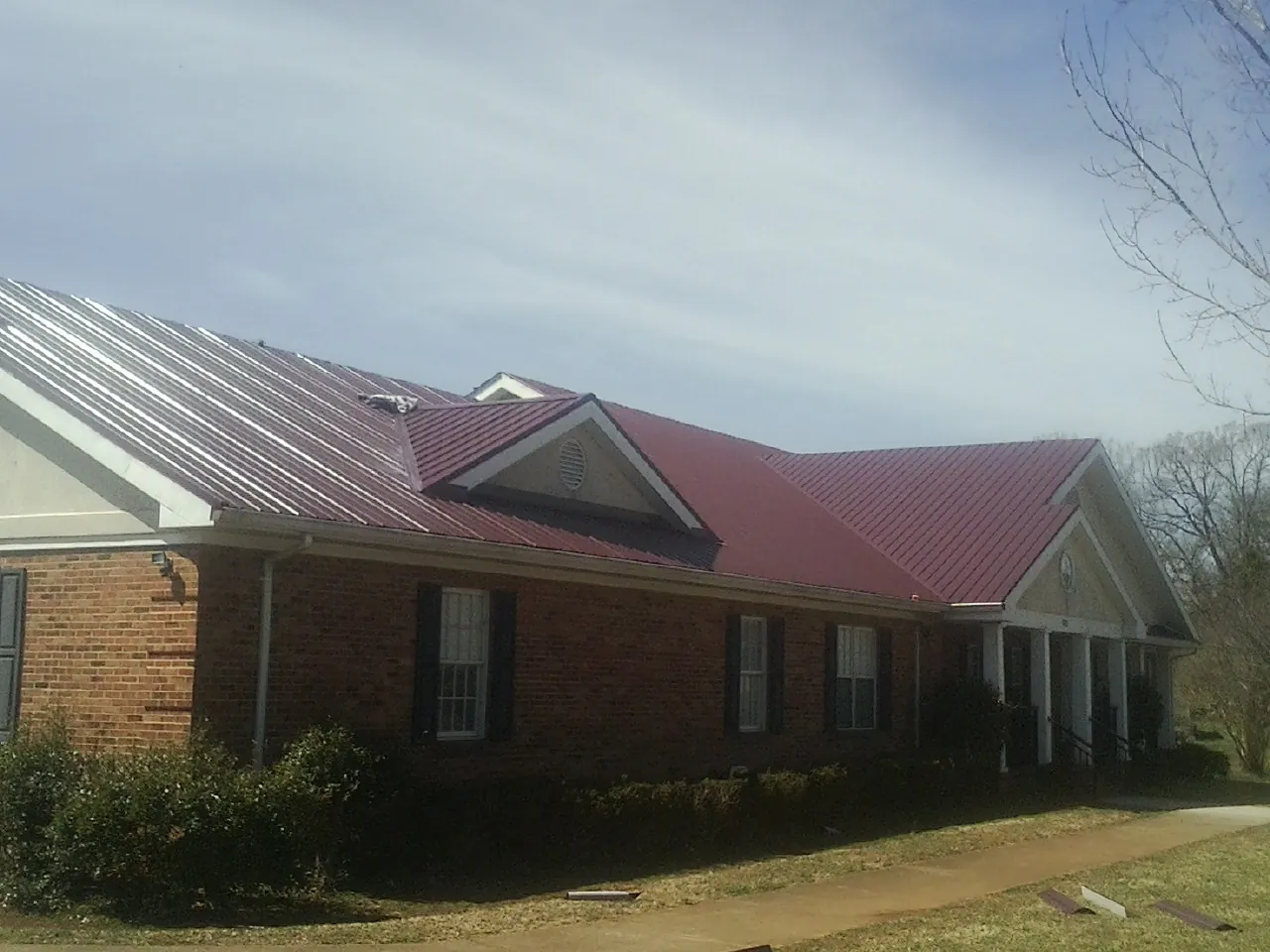 Red metal roof with gabled entries on a long brick building, from a Hail Damage Roof Repair job in Woodburn