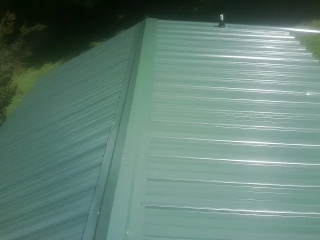 New green metal panels meeting at the ridge of a roof — Flat Roof Repair work by our crew in Woodburn